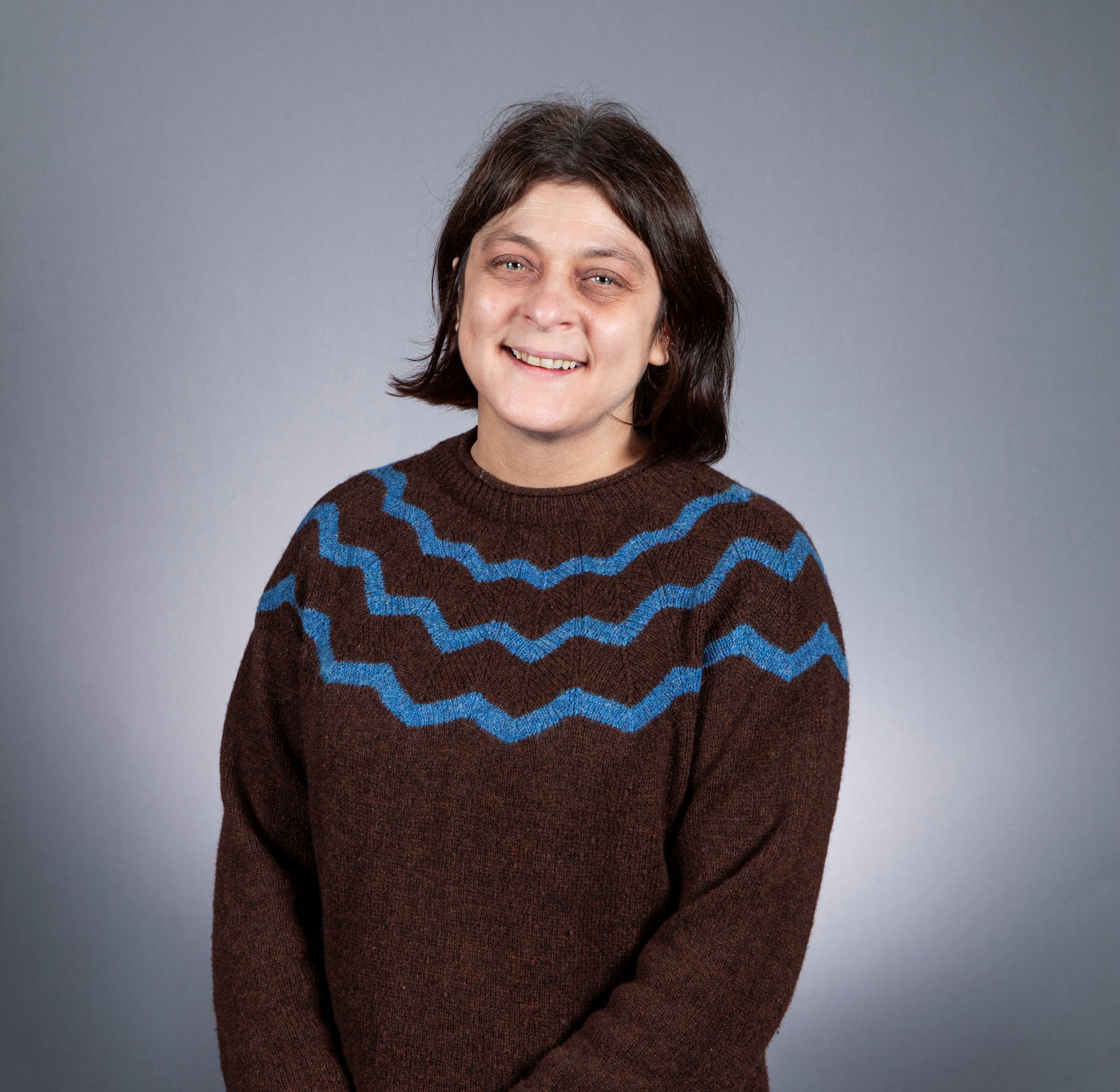 Jenny Gibson headshot wearing brown jumper with zig zag design