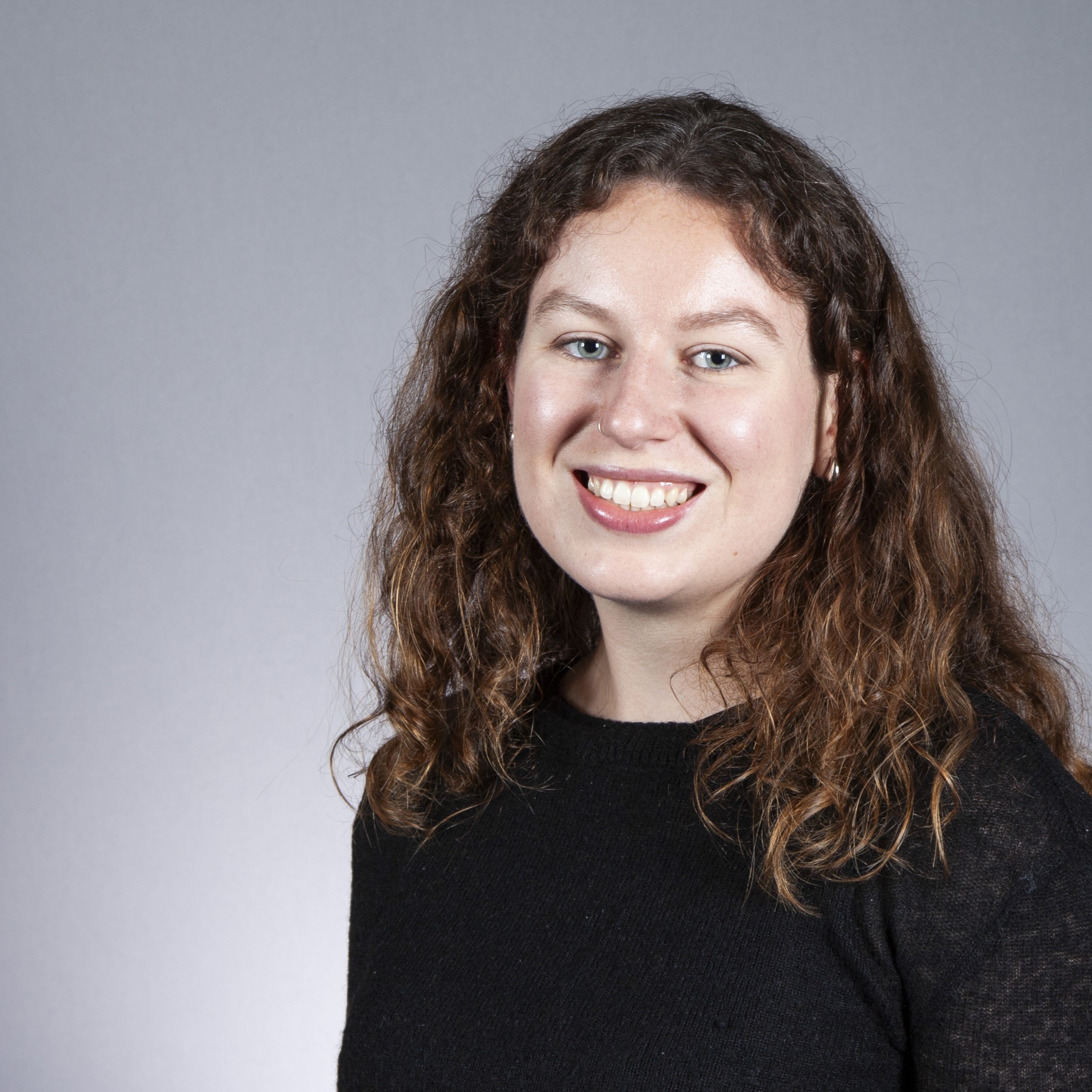 Katie Mennis headshot wearing black jumper with long curly hair