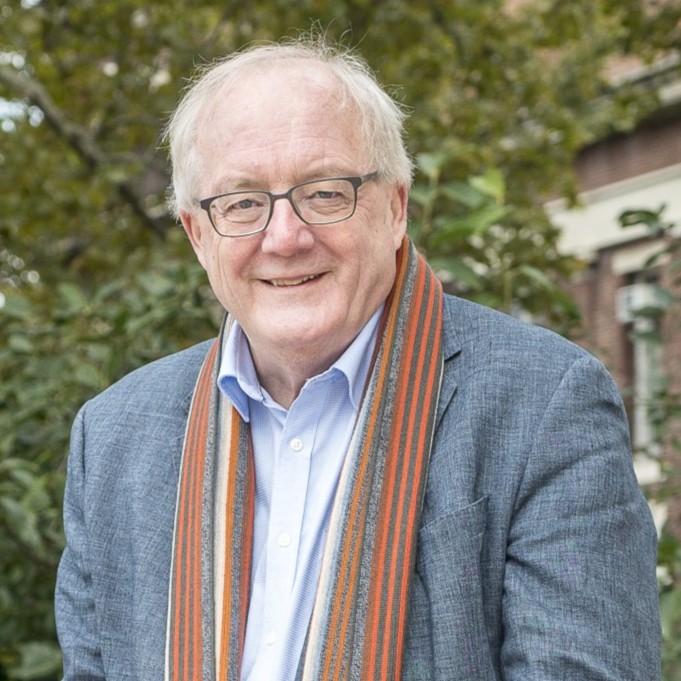 Simon Tavaré headshot, taken outside, wearing grey suit and grey and orange scarf