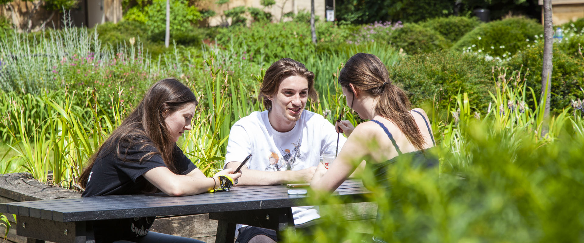 Three people sitting in a garden around a picnic table