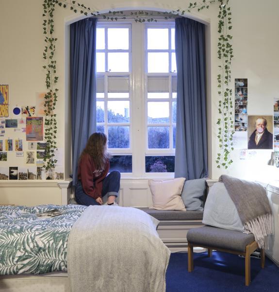 Person sitting looking out of a window, bed in foreground