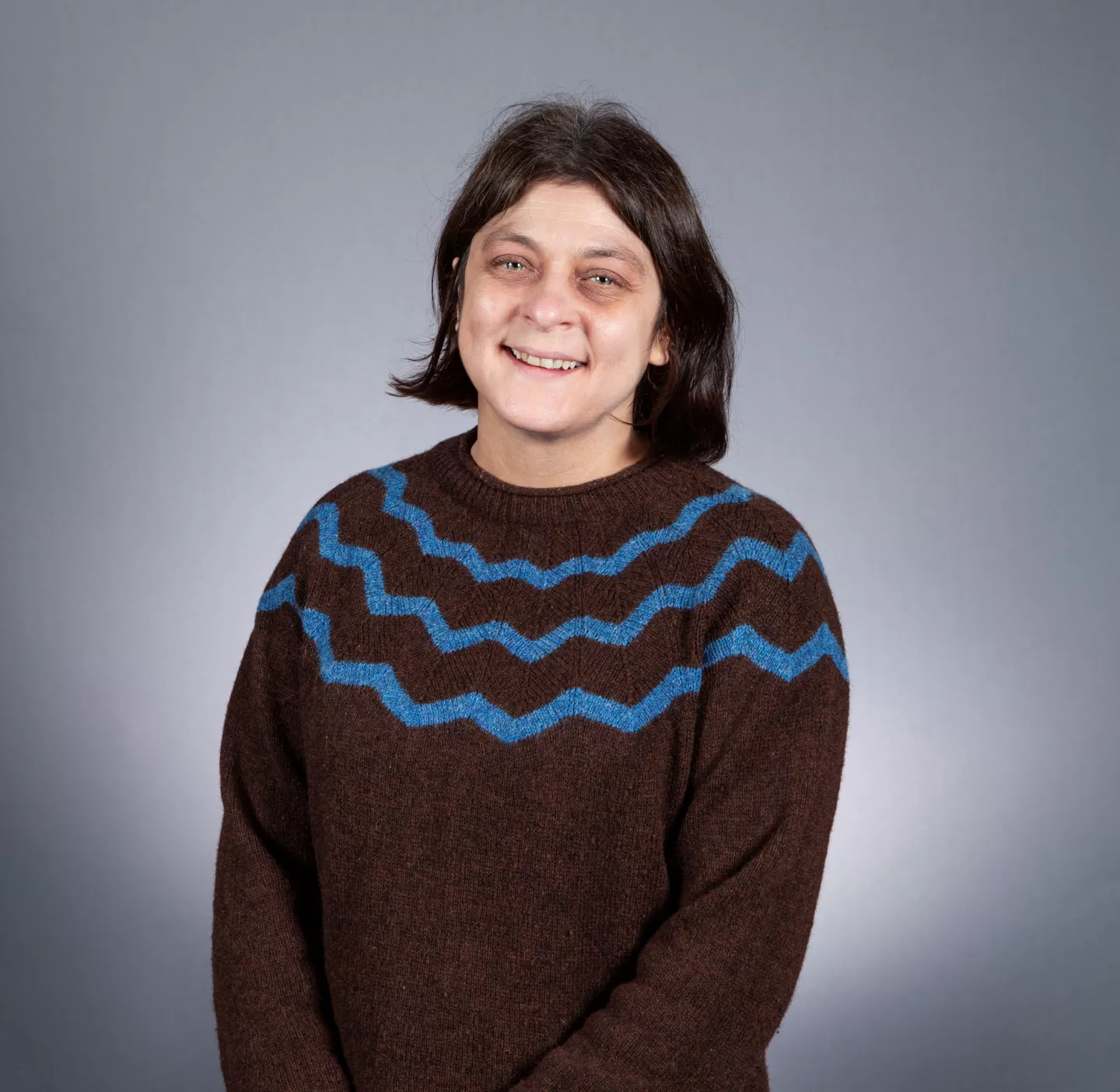 Jenny Gibson headshot wearing brown jumper with zig zag design