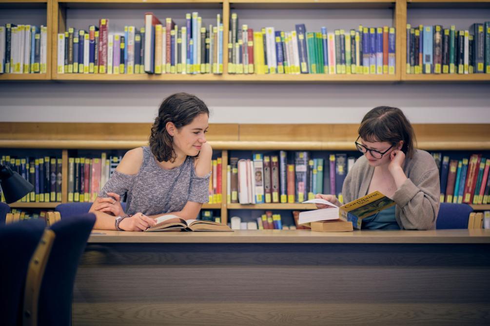 Two smiling students seated in front of bookshelves